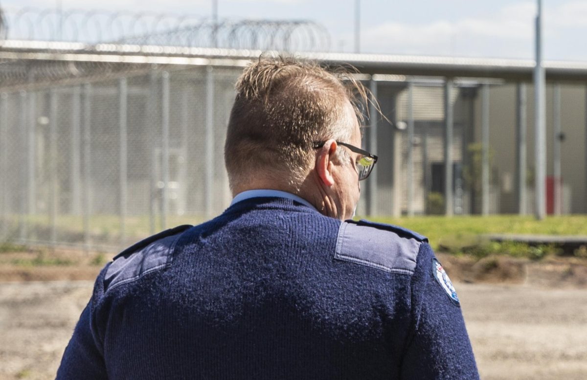 Victorian corrections officer walking along the fence line of a prison, with his back to the camera