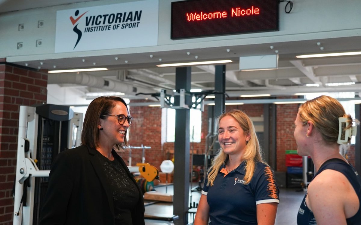 a woman speaking with two female athletes in a gym 