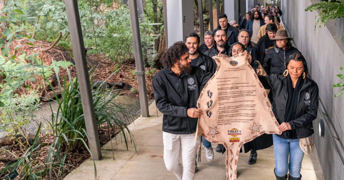 A group of Indigenous people holding animal skin with writing on it regarding their proposed Treaty with the Victorian Government.