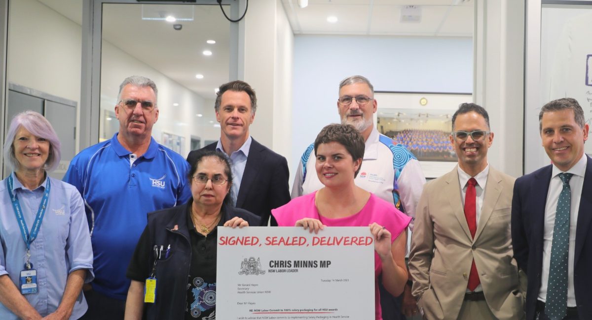 HSU secretary Gerard Hayes, Premier Chris Minns, Treasurer Daniel Mookhey, Health Minister Ryan Park and HSU delegates standing together, with a lady in the front holding up the signed agreement.