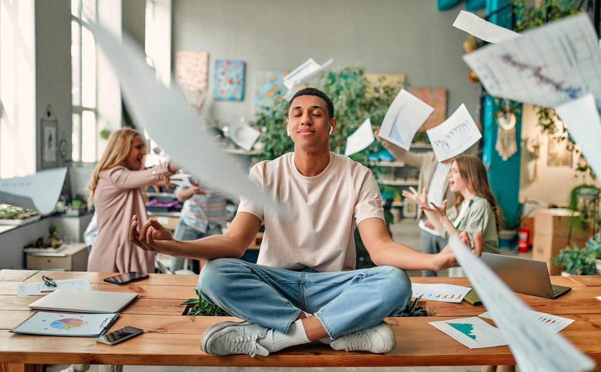 Person sitting cross-legged on a desk amid flying paper