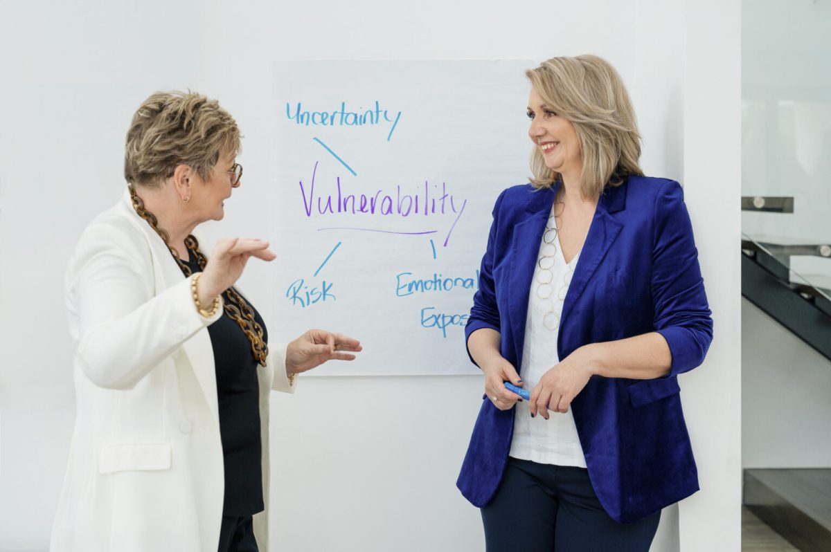 two women speaking with each other in front of a whiteboard