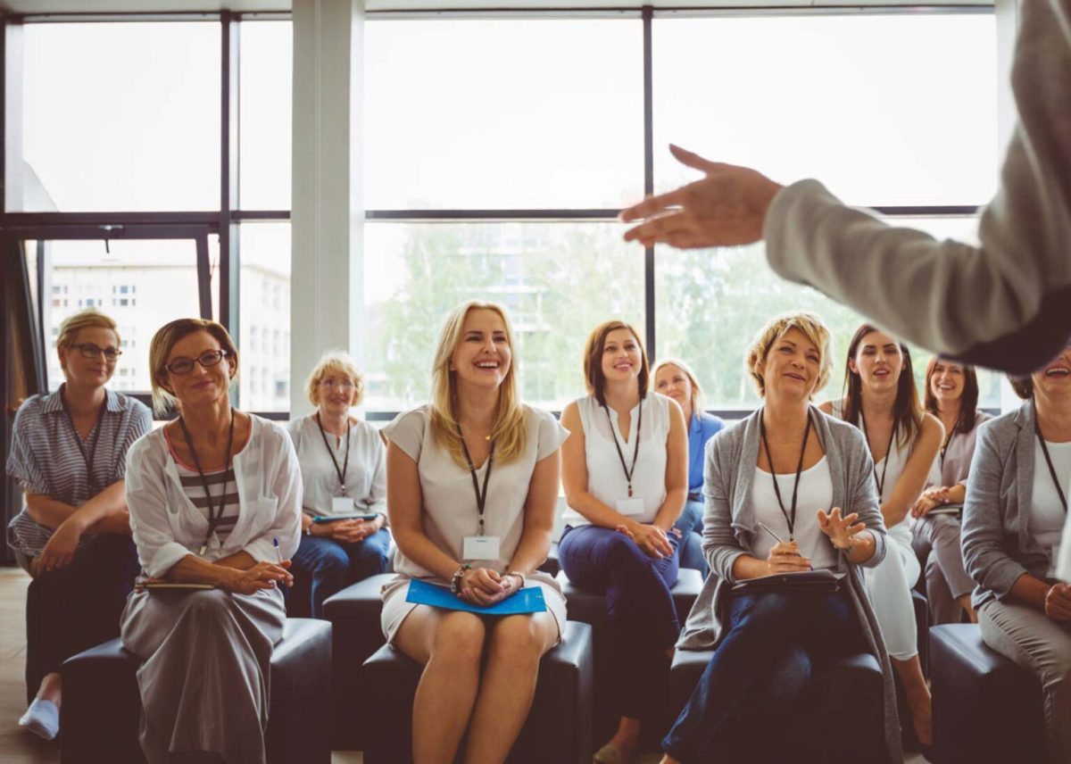 a group of seated women in an office listening to a speaker