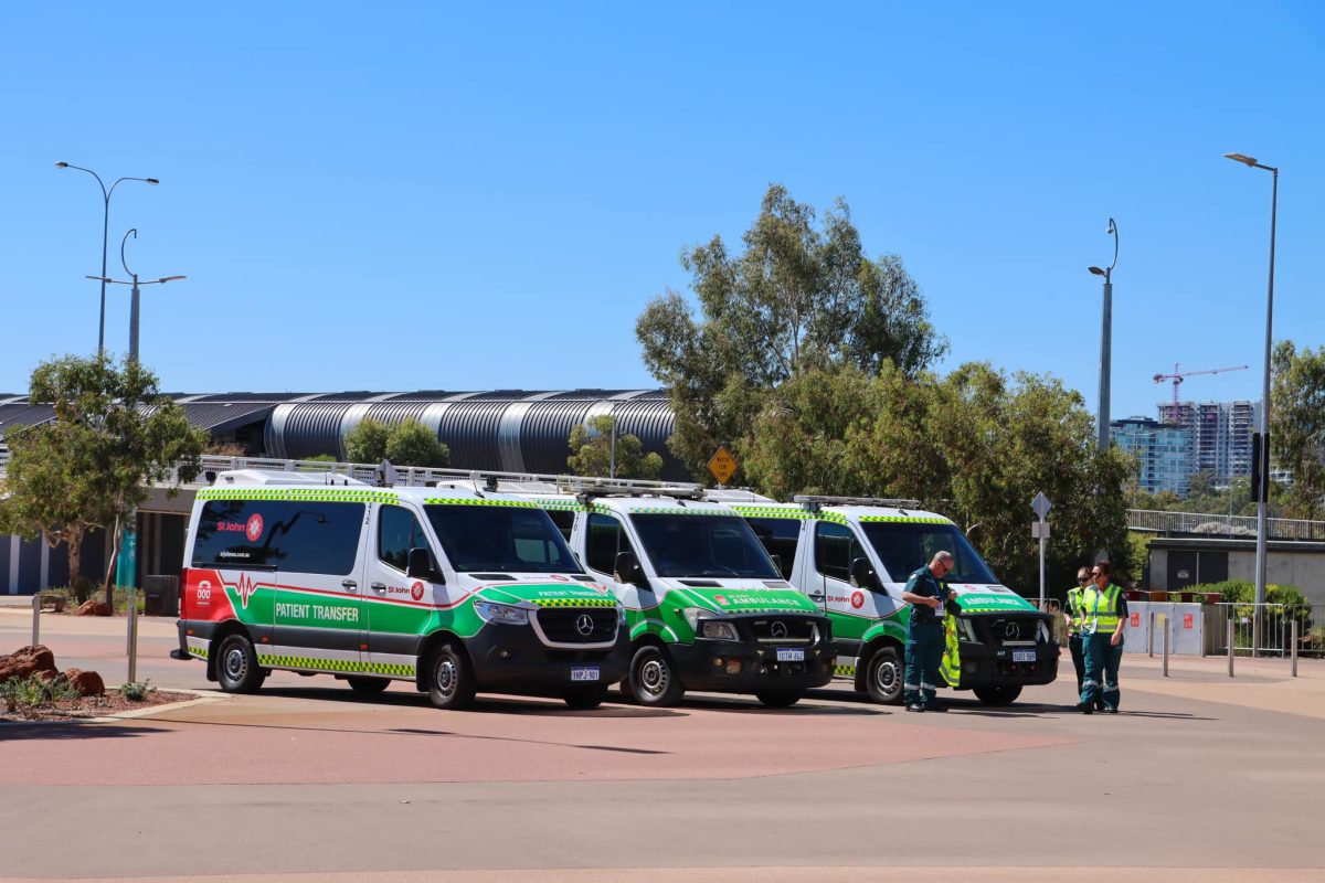 Three St John WA ambulances parked in a carpark with paramedics standing around.