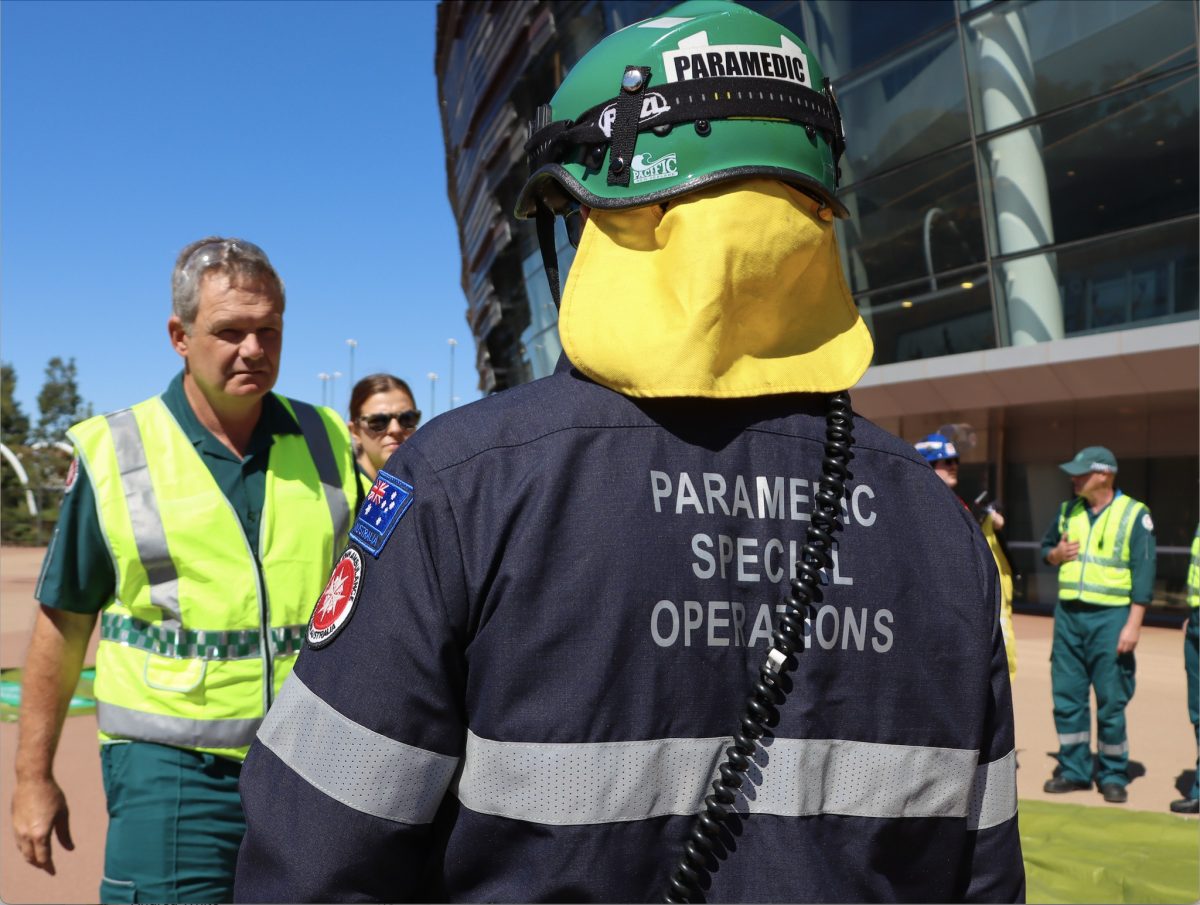 Paramedics talking to each other, one with his back to the camera while wearing a hard hat and jacket reading 'Paramedic Special Operations'.