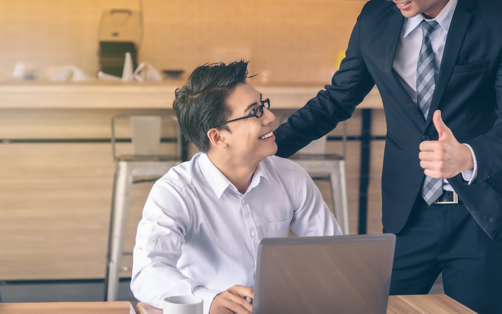 Person at desk smiling up at boss praising him