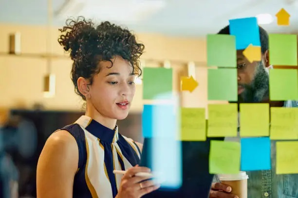 a man and a woman looking at Post-it notes on a glass panel