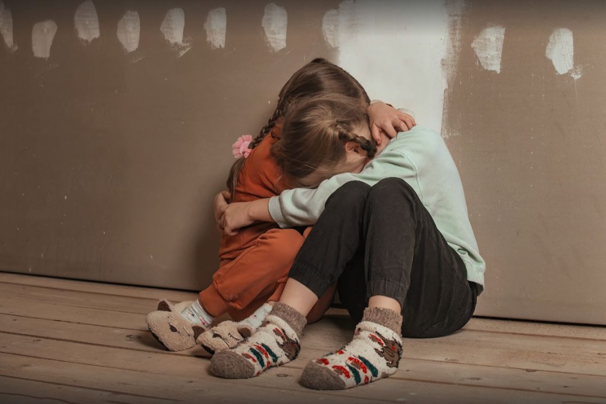 two frightened young girls holding each other against a wall