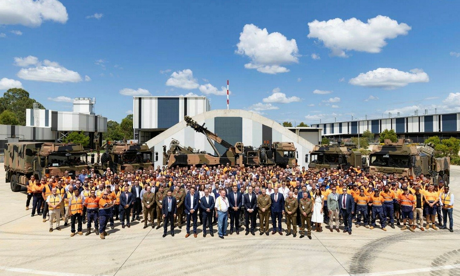 a big group of workers standing in front of army equipment