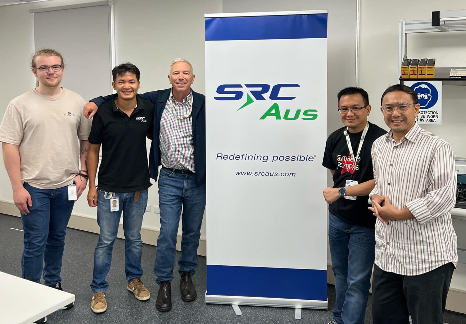 five men standing next to a large company poster