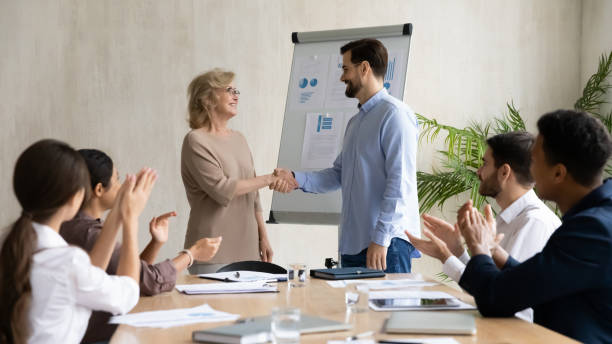 Man and woman shaking hands while others applaud
