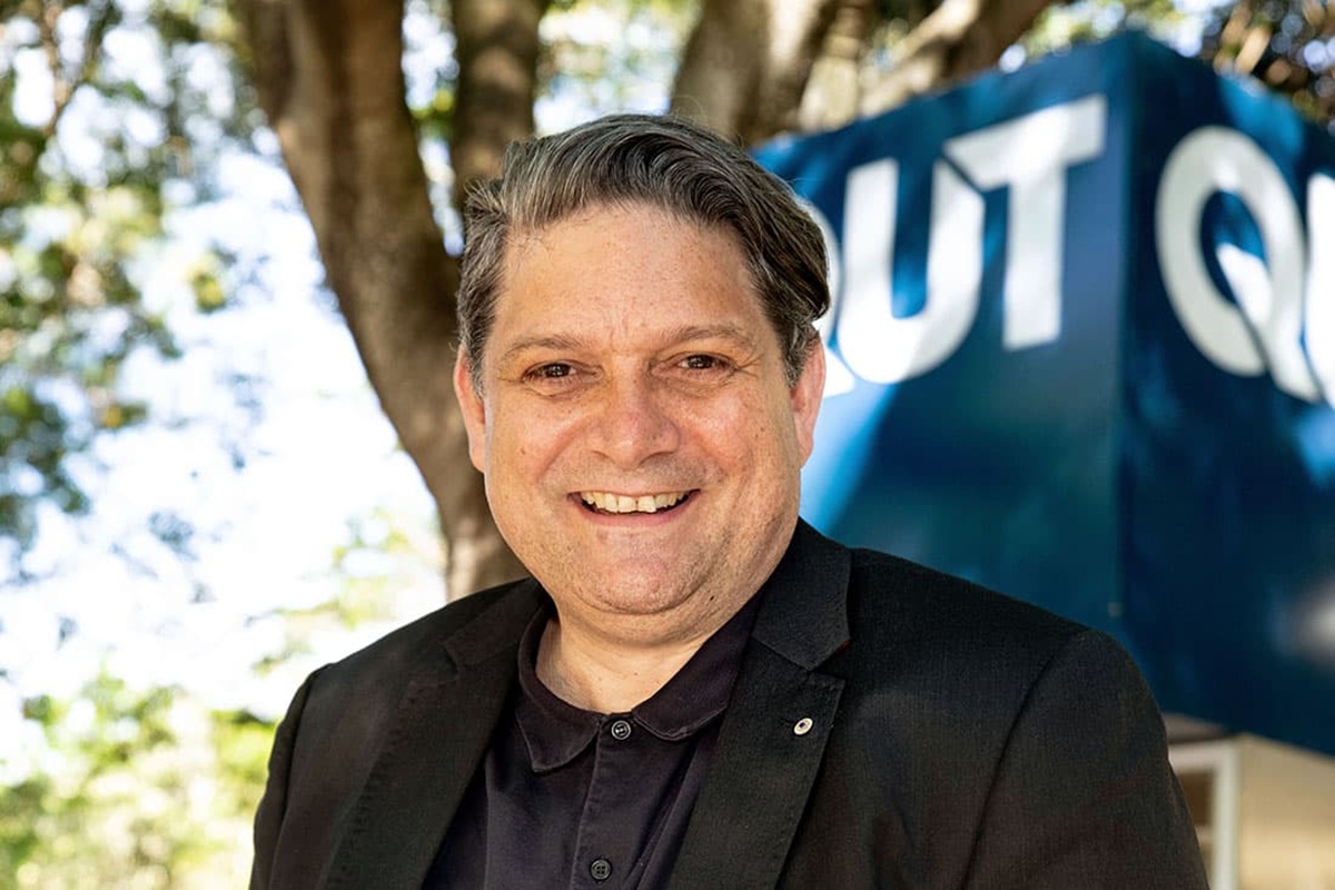 smiling man in front of a QUT sign