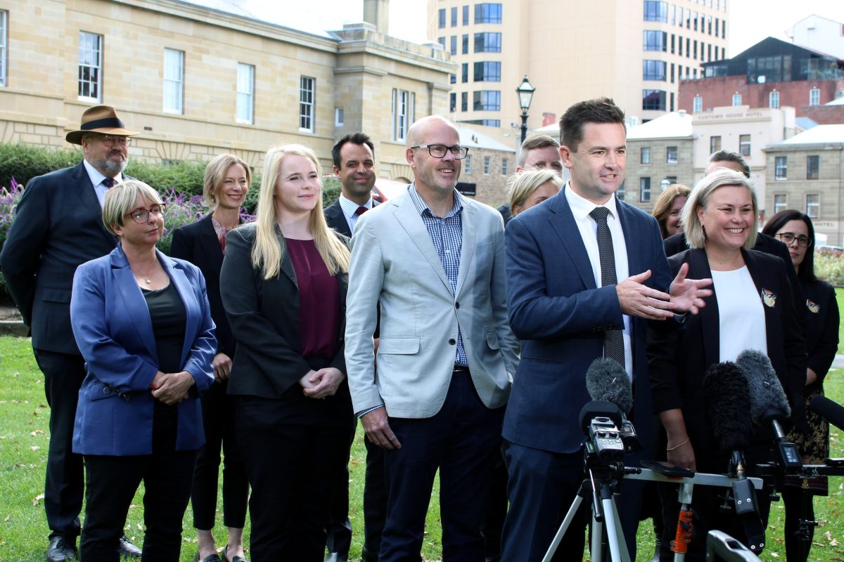 a man giving an outdoor press conference, with colleagues behind him