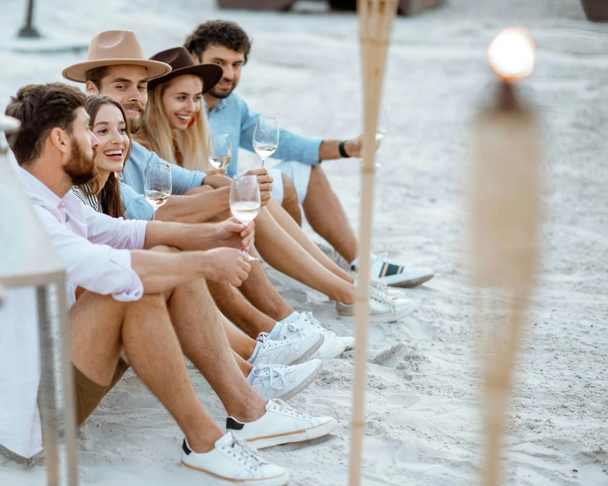 a group of young people drinking wine while sitting on a beach