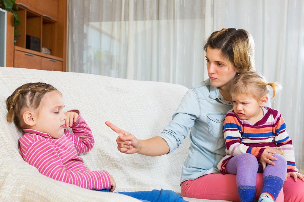 Mother sitting on sofa and scolding little daughter