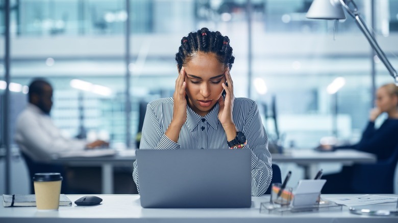Woman at desk holds head in hands