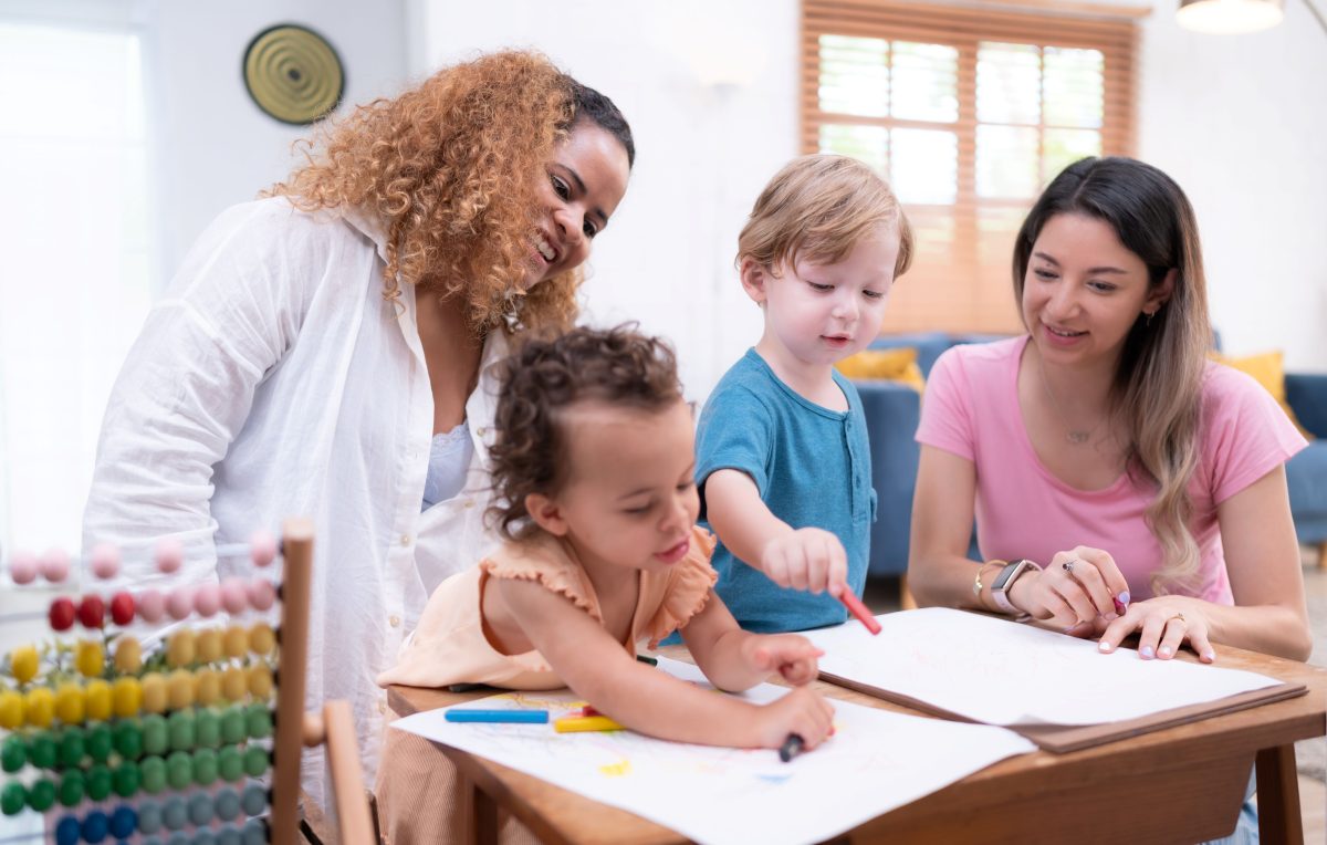 two women with two preschool children drawing in a classroom
