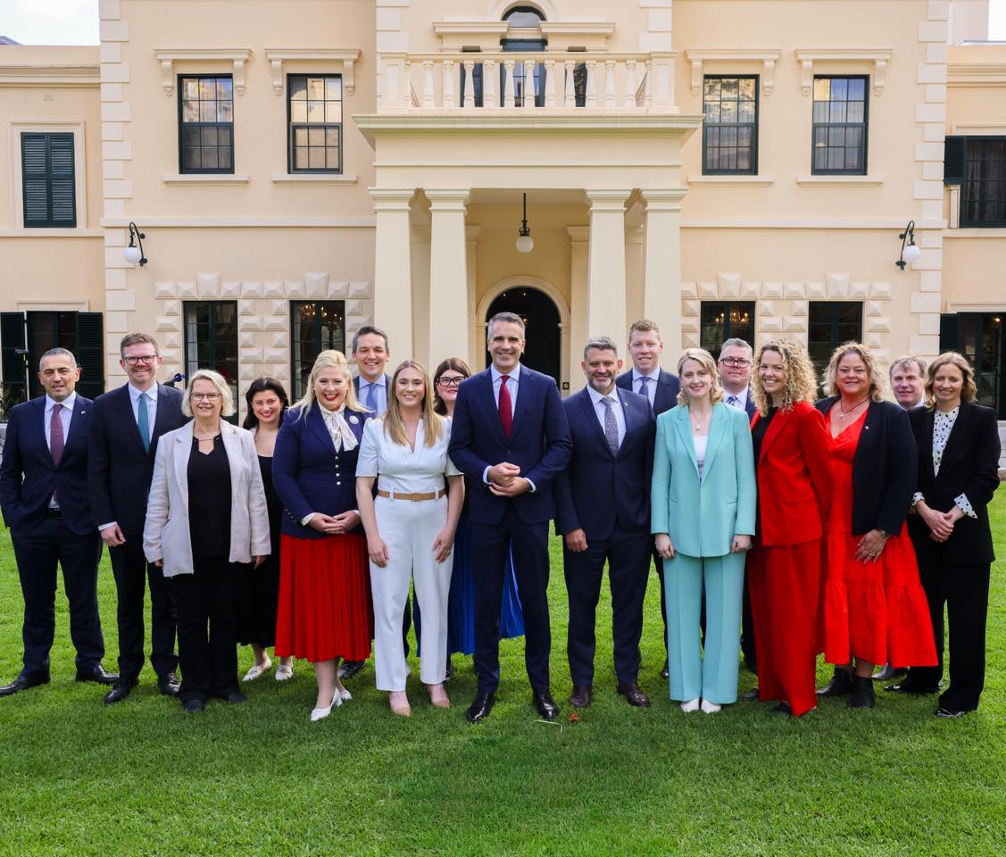 A group of people in office attire standing on a lawn in front of an old building