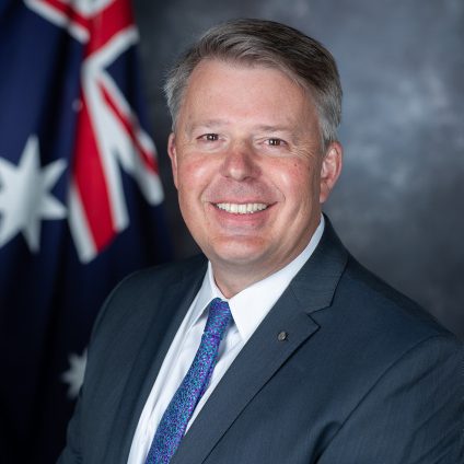 Smiling man in a suit with an Australian flag behind him