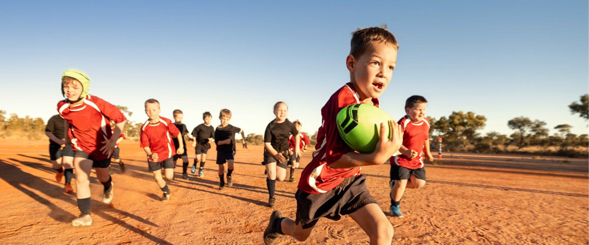 a boy running with a football and being chased by other boys