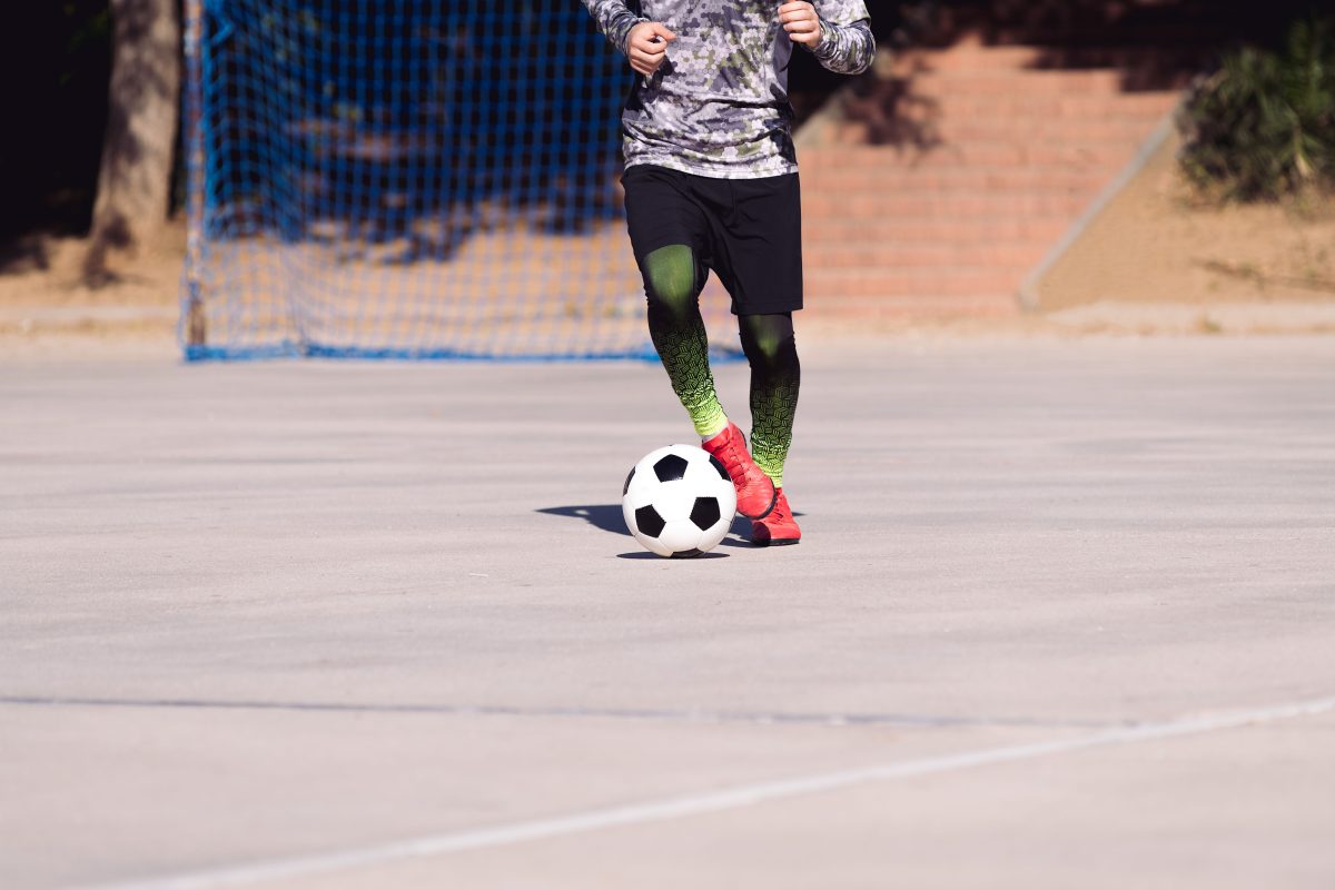 man with a soccer ball at his feet on a concrete pitch