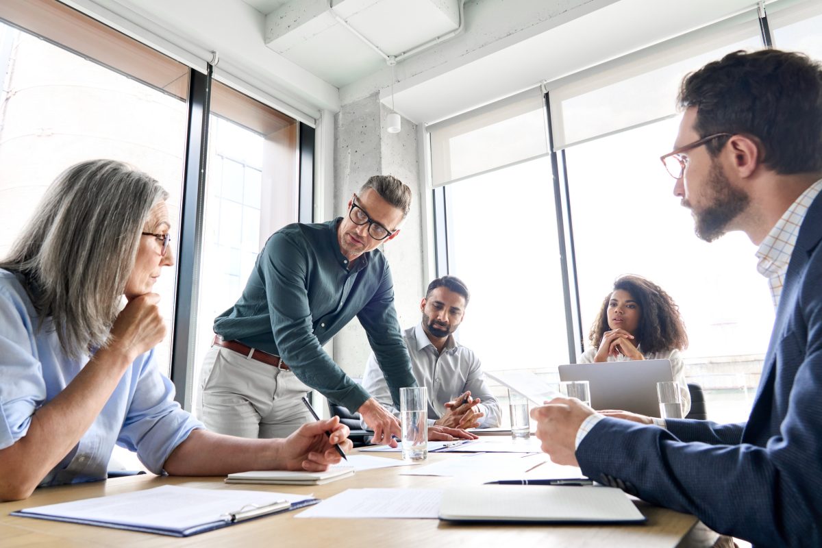 Standing man leading a discussion round a table.