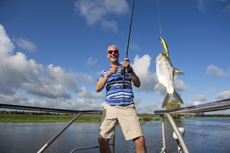A smiling man landing a fish on a boat on a river