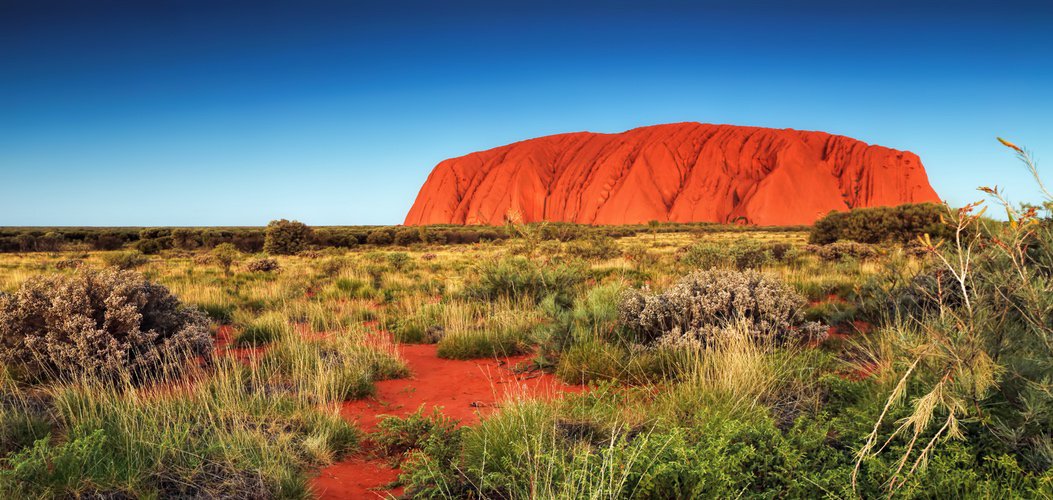 massive red sandstone rock towering above a national park in the outback