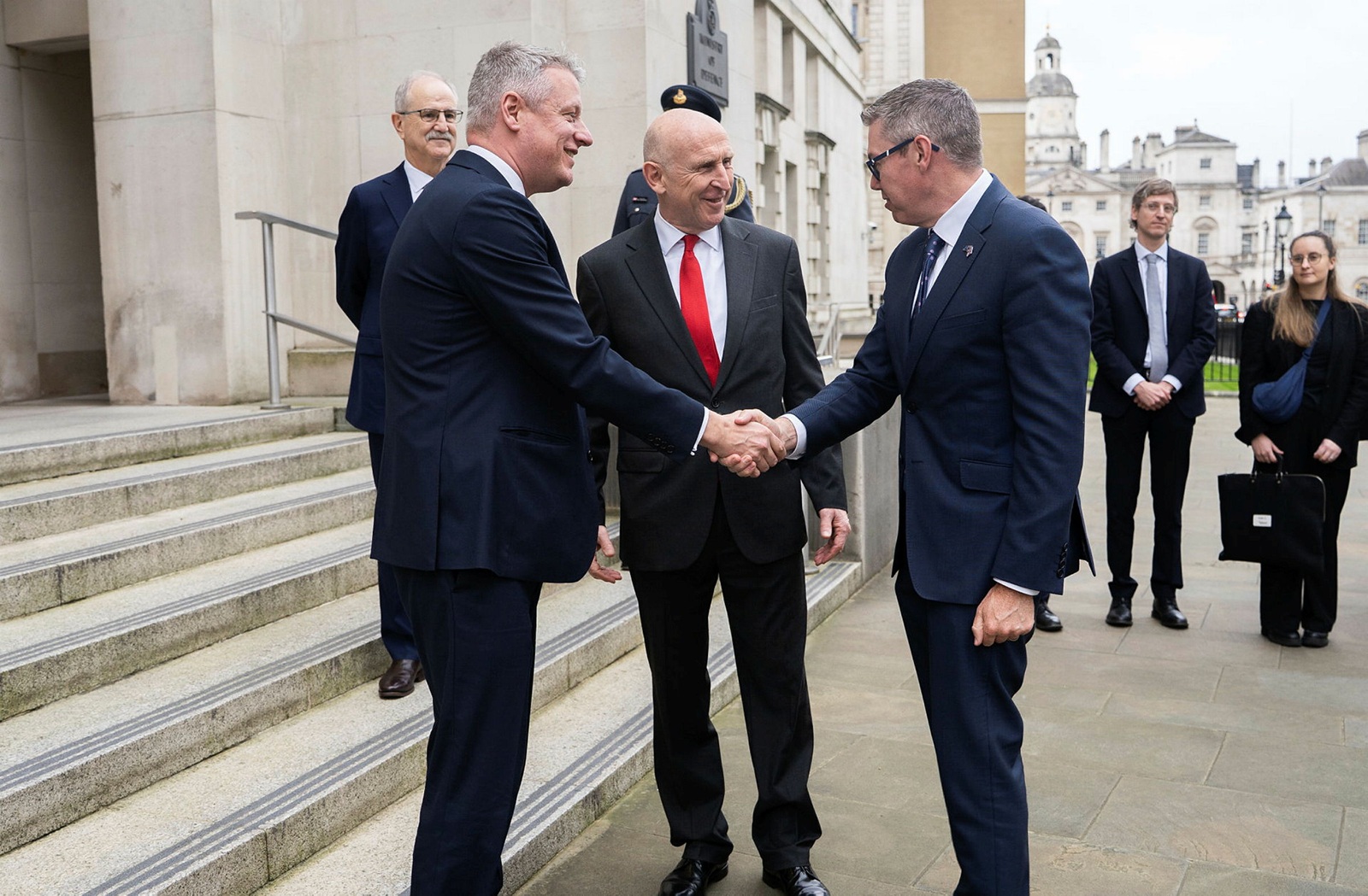 two men in suits shaking hands while other people look on